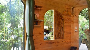 Una cabaña de madera con una ventana, una silla, una cesta roja y un par de pantuflas en el suelo.
