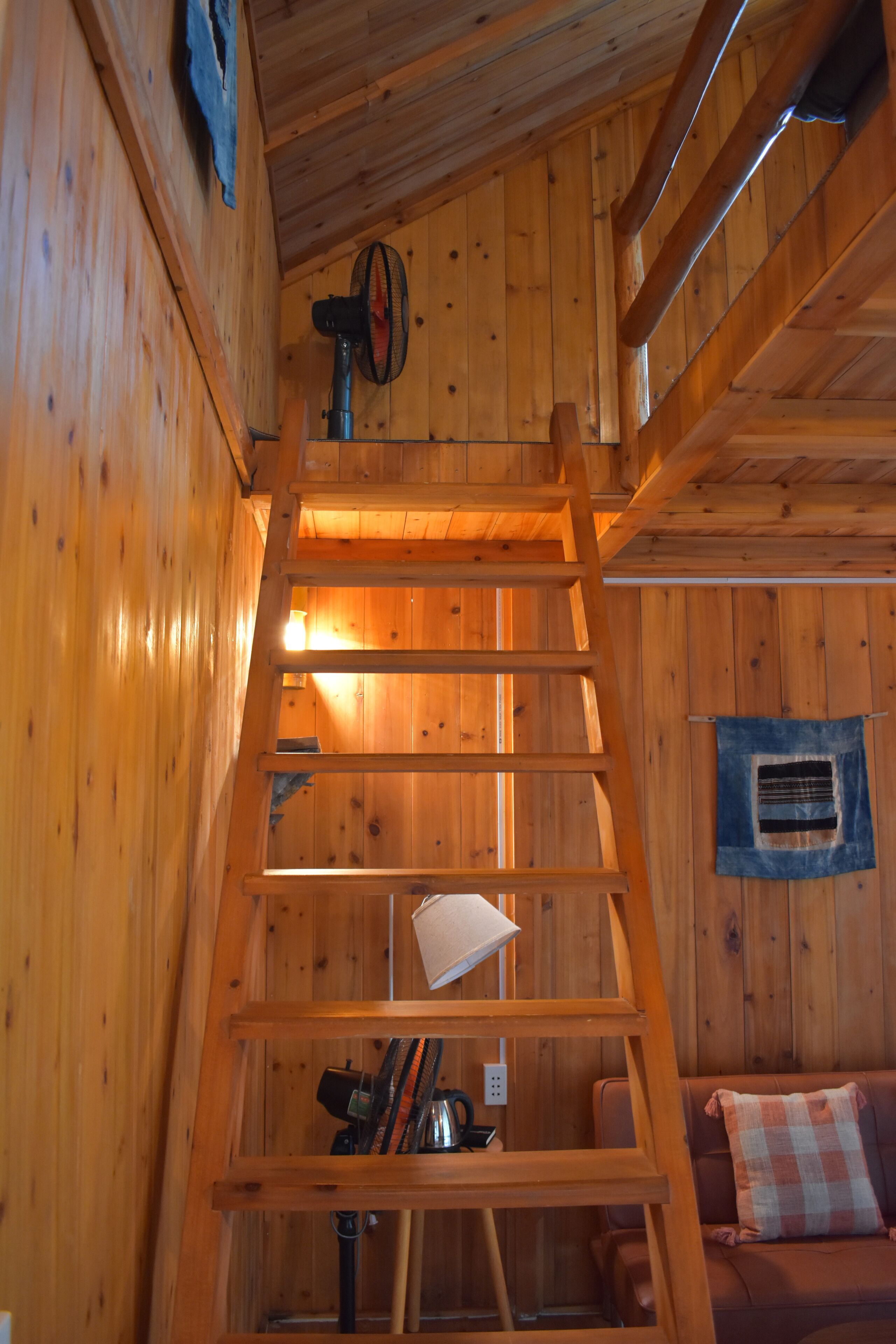Un intérieur en bois avec une échelle en bois, un canapé et un ventilateur fixé au mur.
