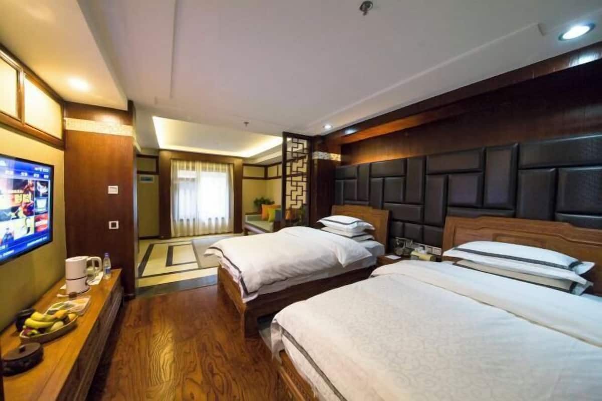 A hotel room with two beds, a TV, a desk with a coffee maker, and a decorative wall panel.