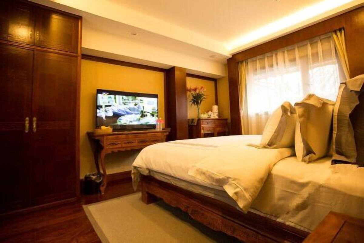 A hotel room with a bed, a television, a wooden wardrobe, and a window with curtains.