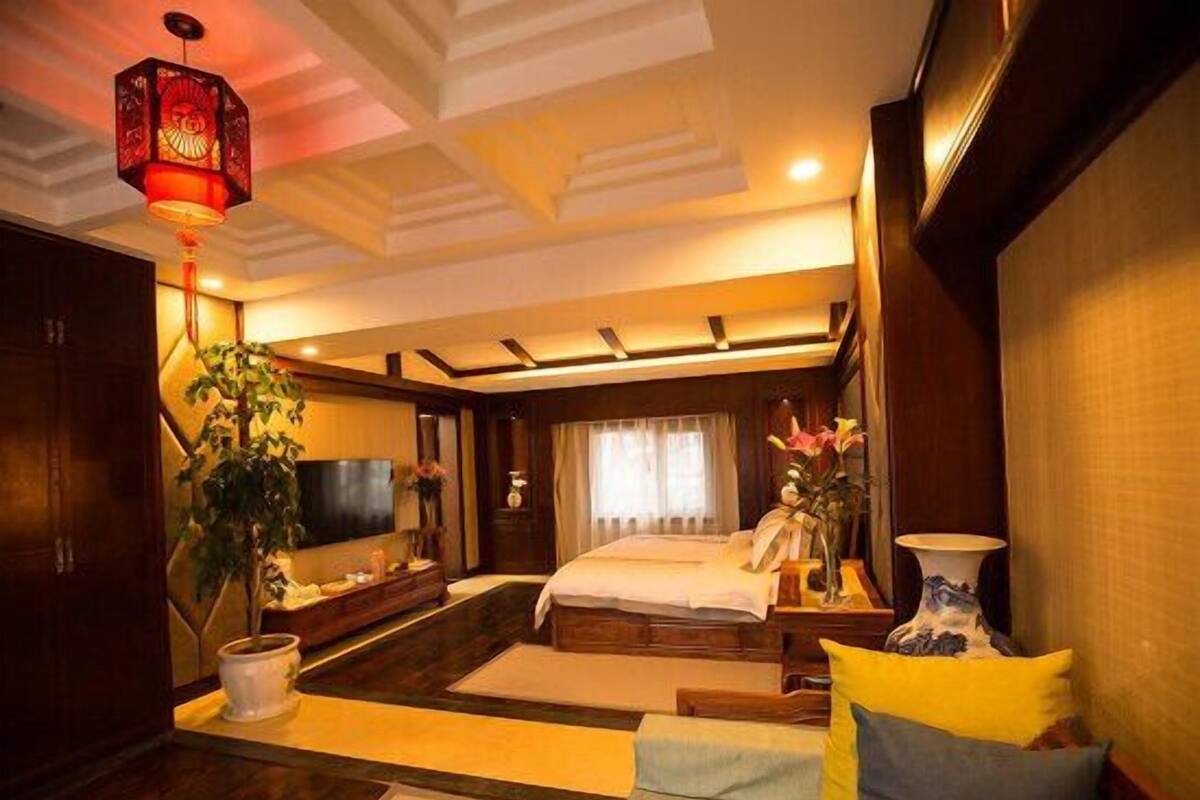 A modern hotel room with a large bed, a TV, a desk, and a plant.