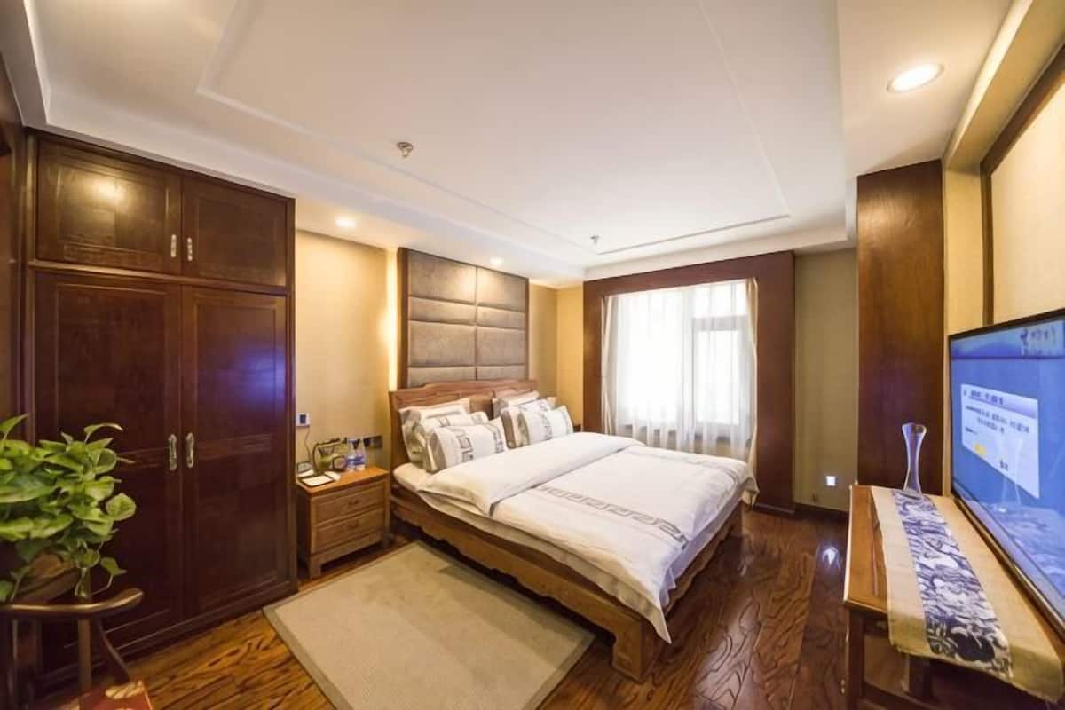 A bedroom with a large bed, wooden wardrobe, bedside table, and a television.