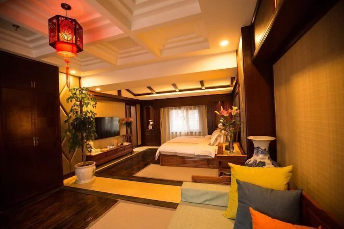 A modern hotel room with a large bed, a TV, a desk, and a plant.