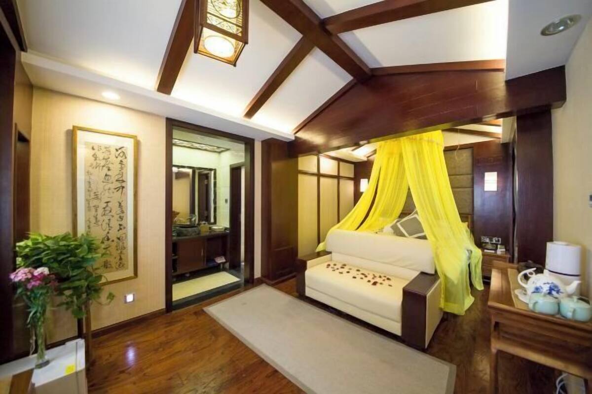 A traditional Japanese-style room with a low wooden ceiling, a bed with a yellow canopy, a large framed calligraphy piece on the wall, and a wooden floor.