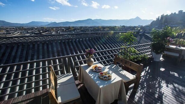 Une terrasse sur le toit, avec une table dressée pour le dîner, offrant une vue sur le paysage urbain et les montagnes.