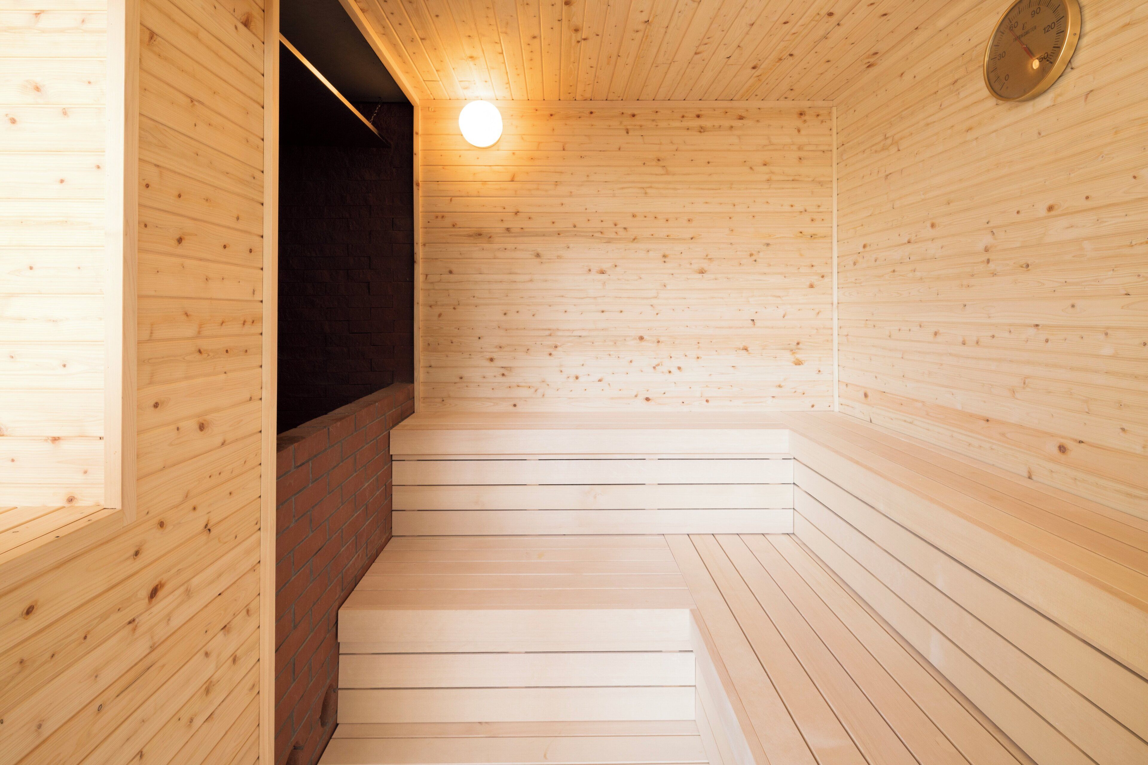 A wooden sauna with a brick wall, a wooden bench, and a round wall clock.