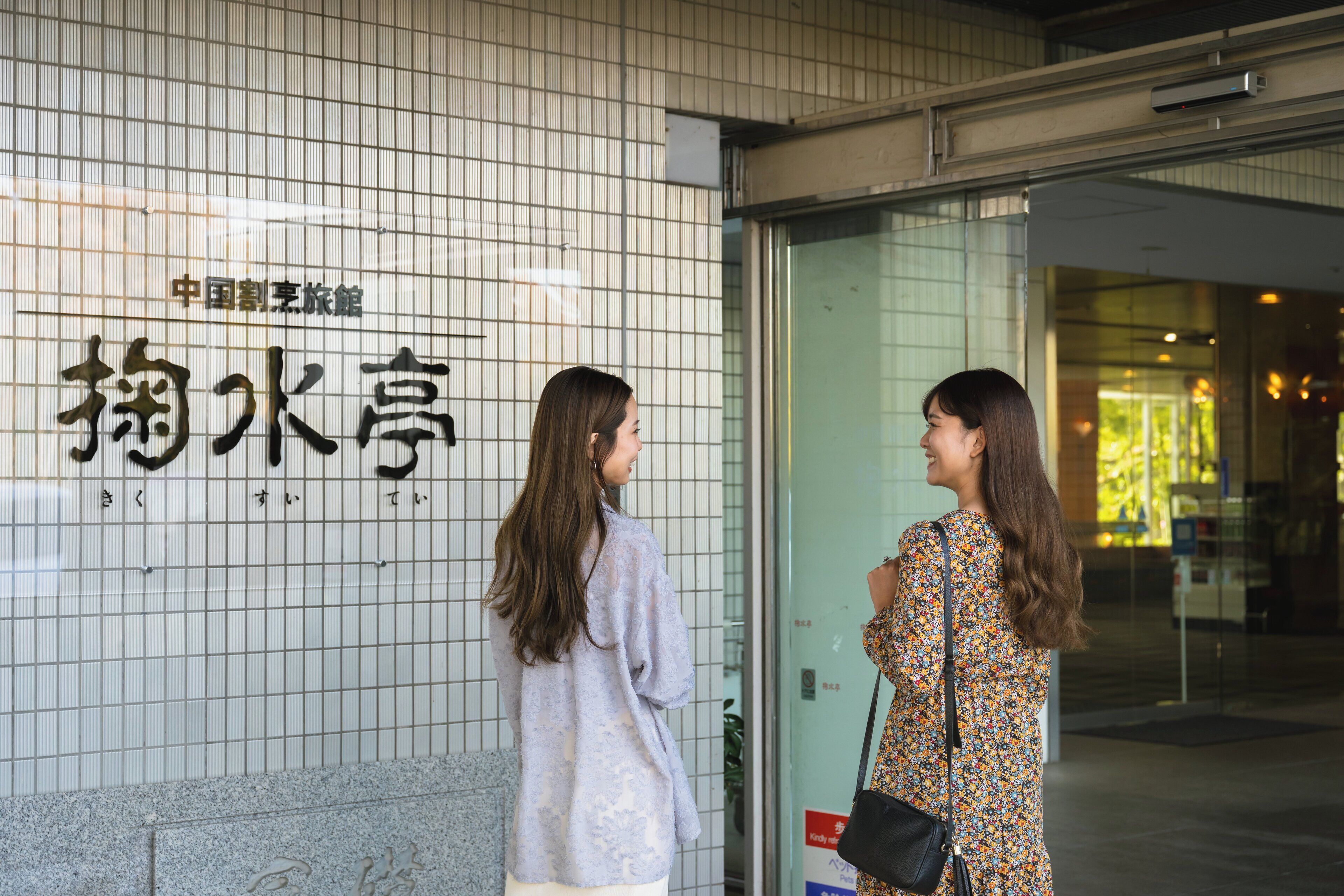 Two women standing in front of a building with a sign that reads "China Cut Flower Hotel."
