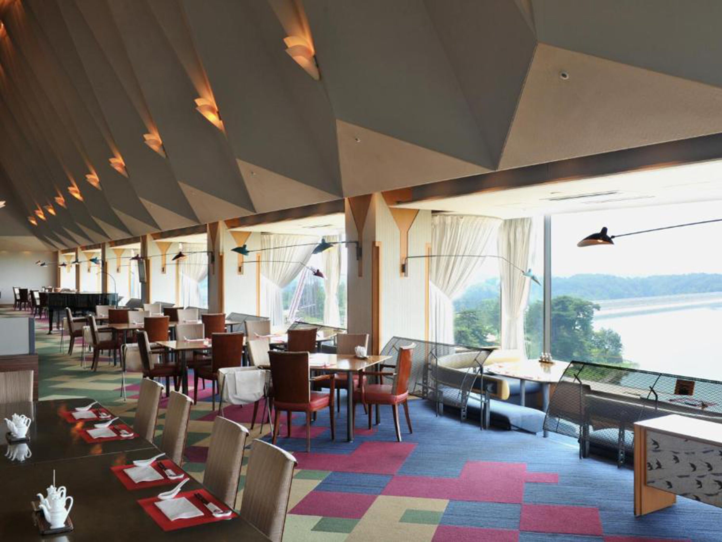 A spacious dining area with tables and chairs, large windows with curtains, and a view of a body of water.