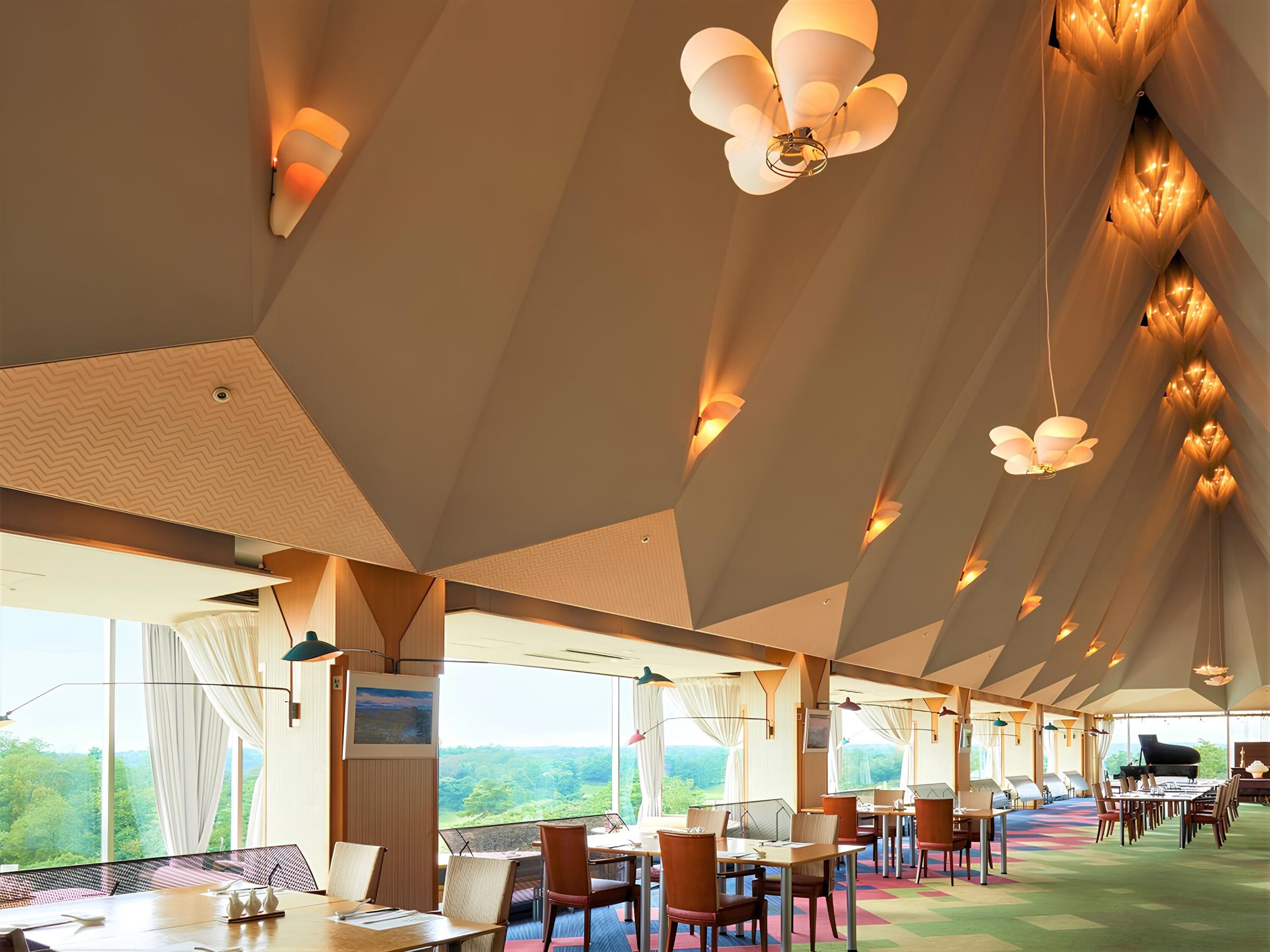 A spacious dining area with tables and chairs, large windows offering a view of the outdoors, and a ceiling with unique lighting fixtures.