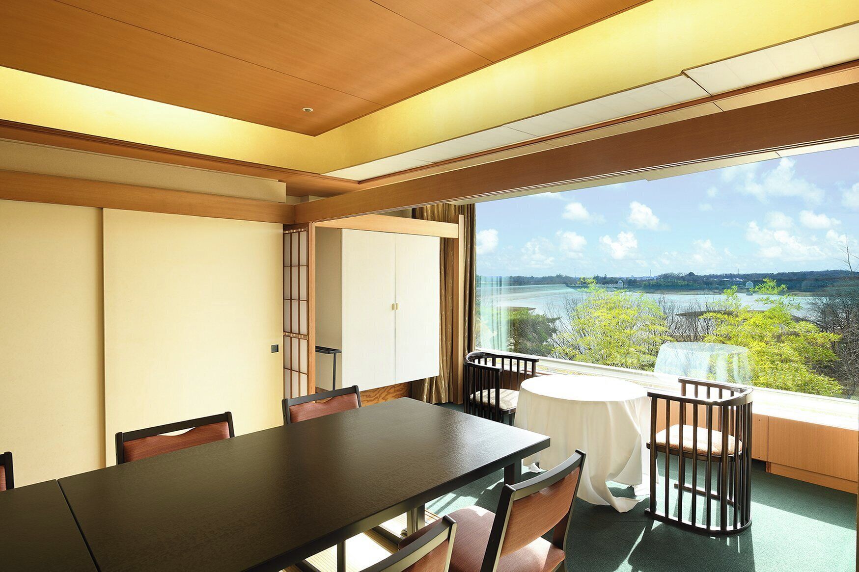 Ein Zimmer mit Esstisch, Stühlen, einem Babybett und einem großen Fenster mit Blick auf Wasser und Grünflächen.