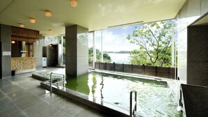 A modern indoor pool with clear glass walls, a wooden reception desk, and a view of a lake. - Kikusuitei (Higashiyamato)