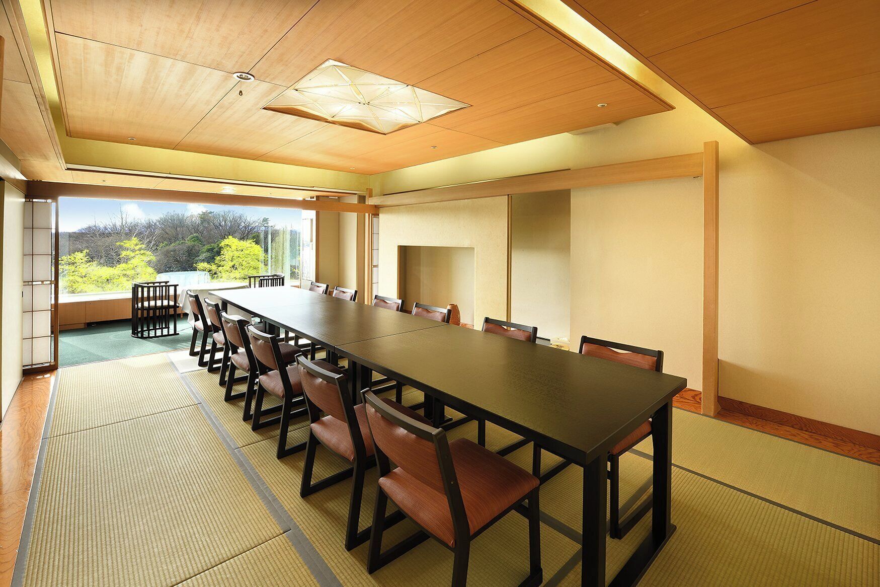 Un salón de conferencias con una larga mesa y sillas, ventanas amplias con vistas a zonas verdes y un techo de madera.