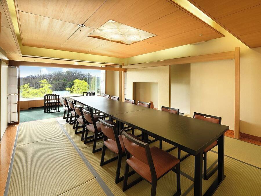 Un salón de conferencias con una larga mesa y sillas, ventanas amplias con vistas a zonas verdes y un techo de madera.
