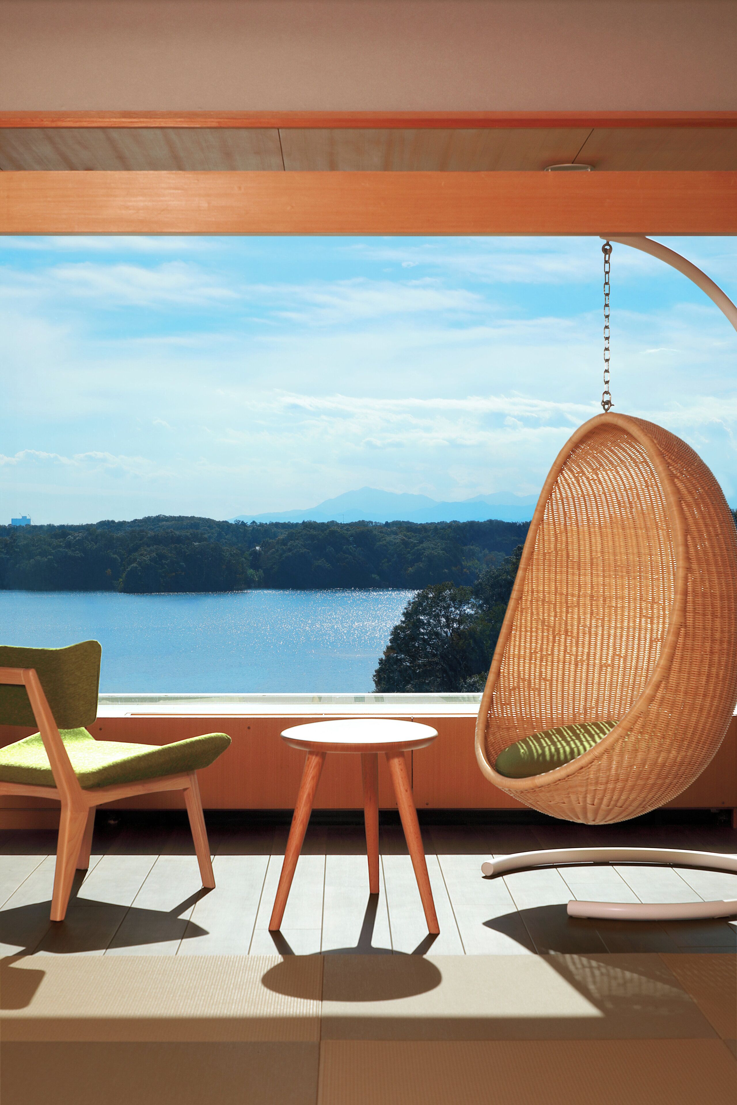 A room with a view of a lake, a hanging chair, and a table.