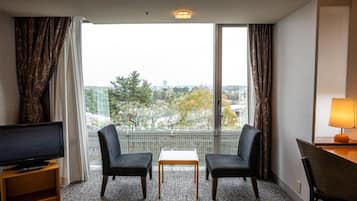 A hotel room with a TV on a stand, two chairs, a small table, and a lamp.