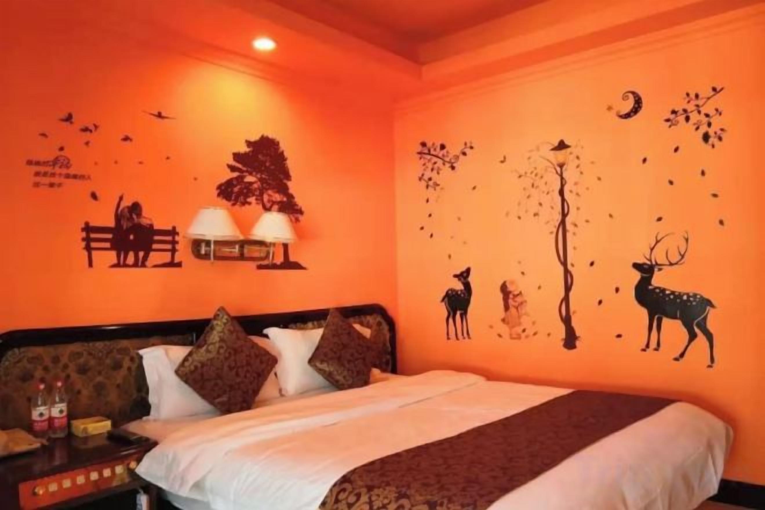 Una habitación con una cama, una mesita de noche y una pared decorada con siluetas de animales y un árbol.