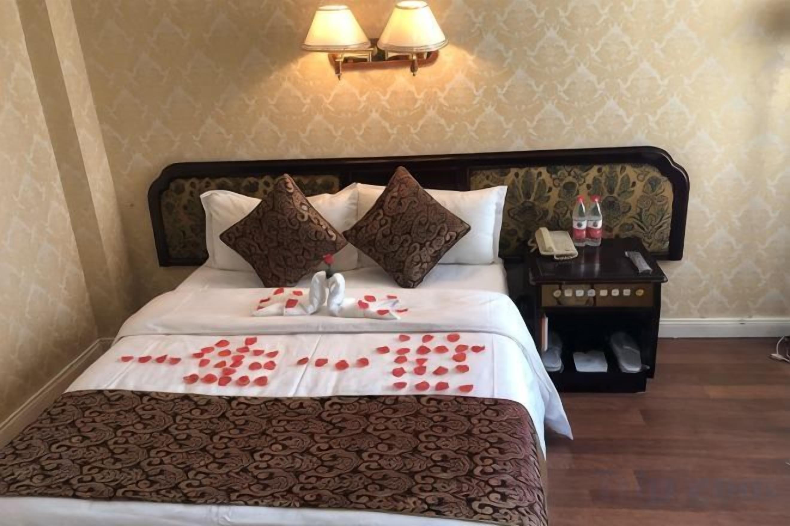 A neatly made bed with a patterned bedspread, two decorative pillows, and a bedside table with a lamp and a bottle.