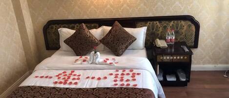A neatly made bed with a patterned bedspread, two decorative pillows, and a bedside table with a lamp and a bottle.