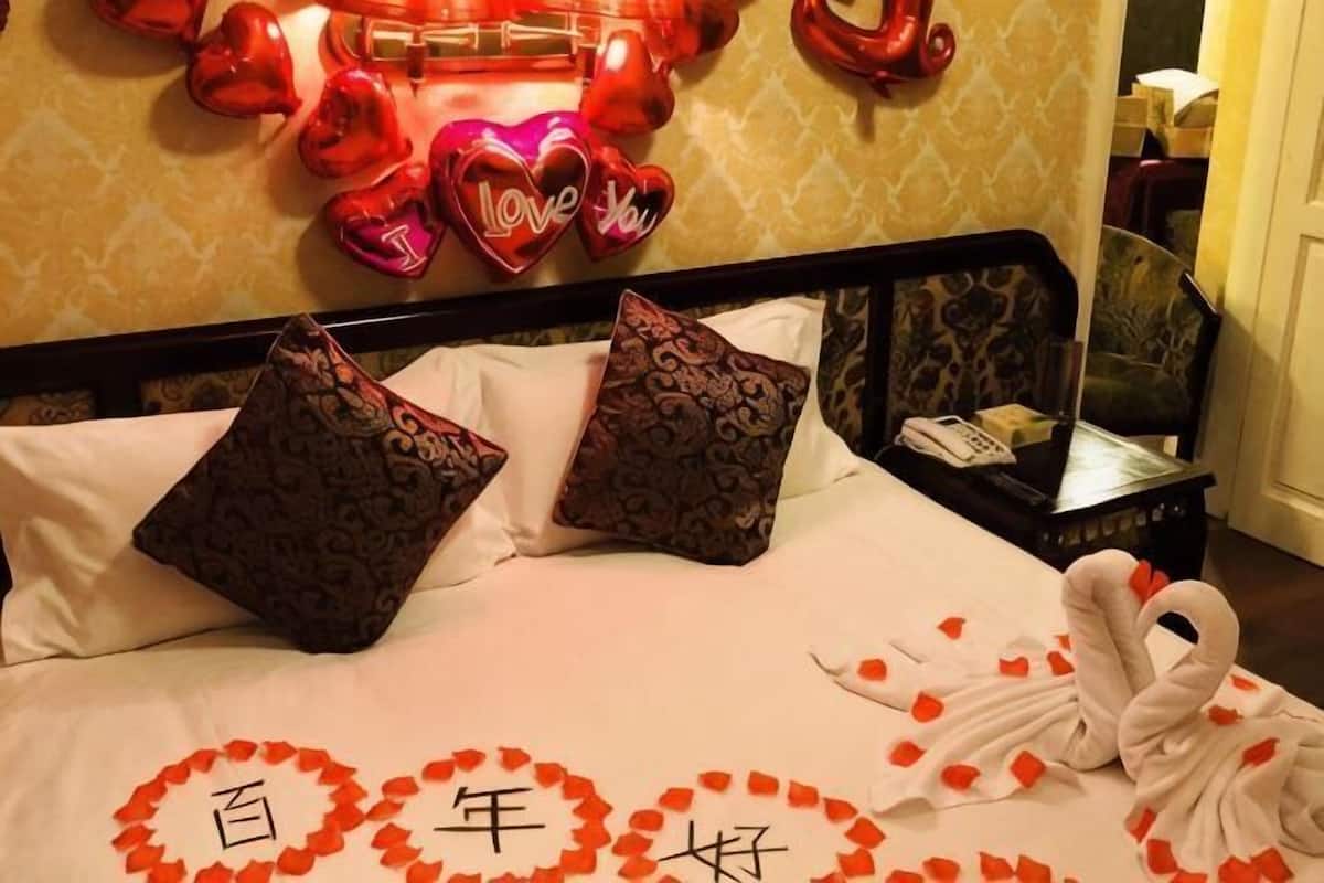 Un lit décoré de motifs en forme de cœur, avec des oreillers et une table de chevet sur laquelle se trouve un téléphone.