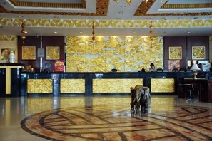A hotel lobby with a reception desk, gold leaf wall art, and a circular marble floor.