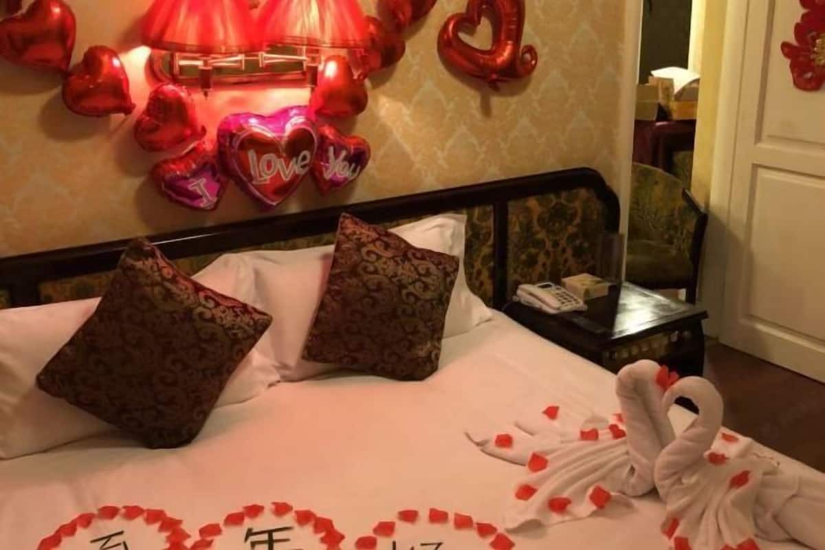 Une chambre d’hôtel avec un lit, des oreillers, une table de chevet et un mur décoré de ballons en forme de cœur.