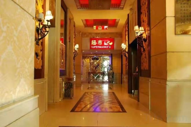 A hotel corridor with a red sign for a supermarket, marble walls, and a patterned carpet.