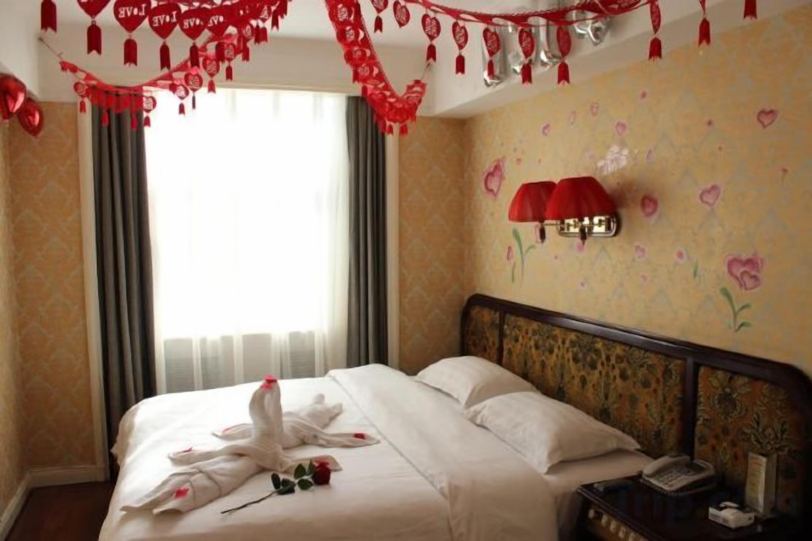Ein Hotelzimmer mit Bett, Nachttisch, Wandlampe und einem Fenster mit Vorhängen.