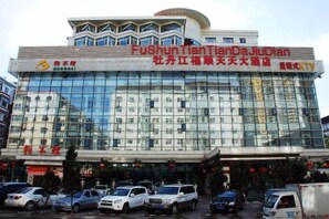 Un edificio de varios pisos con fachada de vidrio, letreros que indican 'Fushun TianDanDaJiaoDian' y varios vehículos estacionados en la parte delantera.