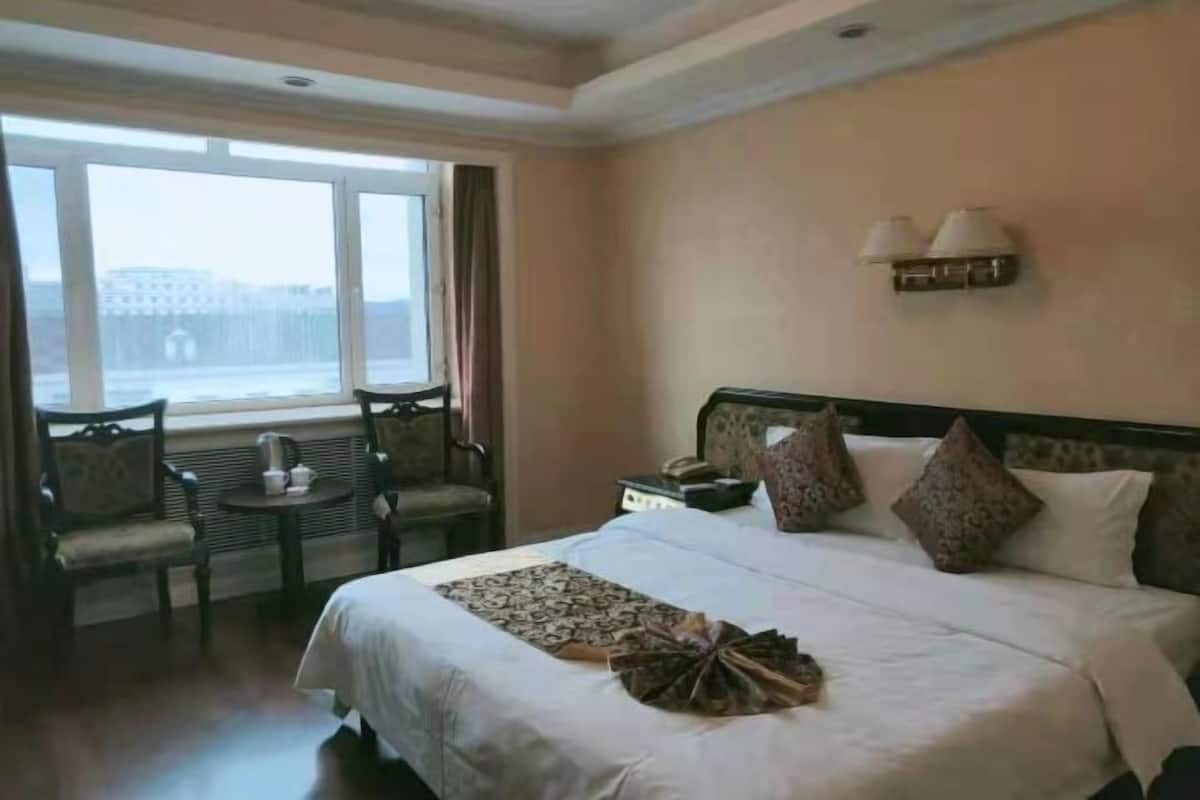 Une chambre d’hôtel avec un grand lit, deux chaises, une petite table, une table de chevet et une fenêtre avec des rideaux.