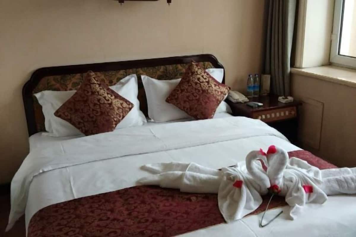 Une chambre d’hôtel avec un lit, des oreillers, une table de chevet avec un téléphone et une fenêtre avec des rideaux.