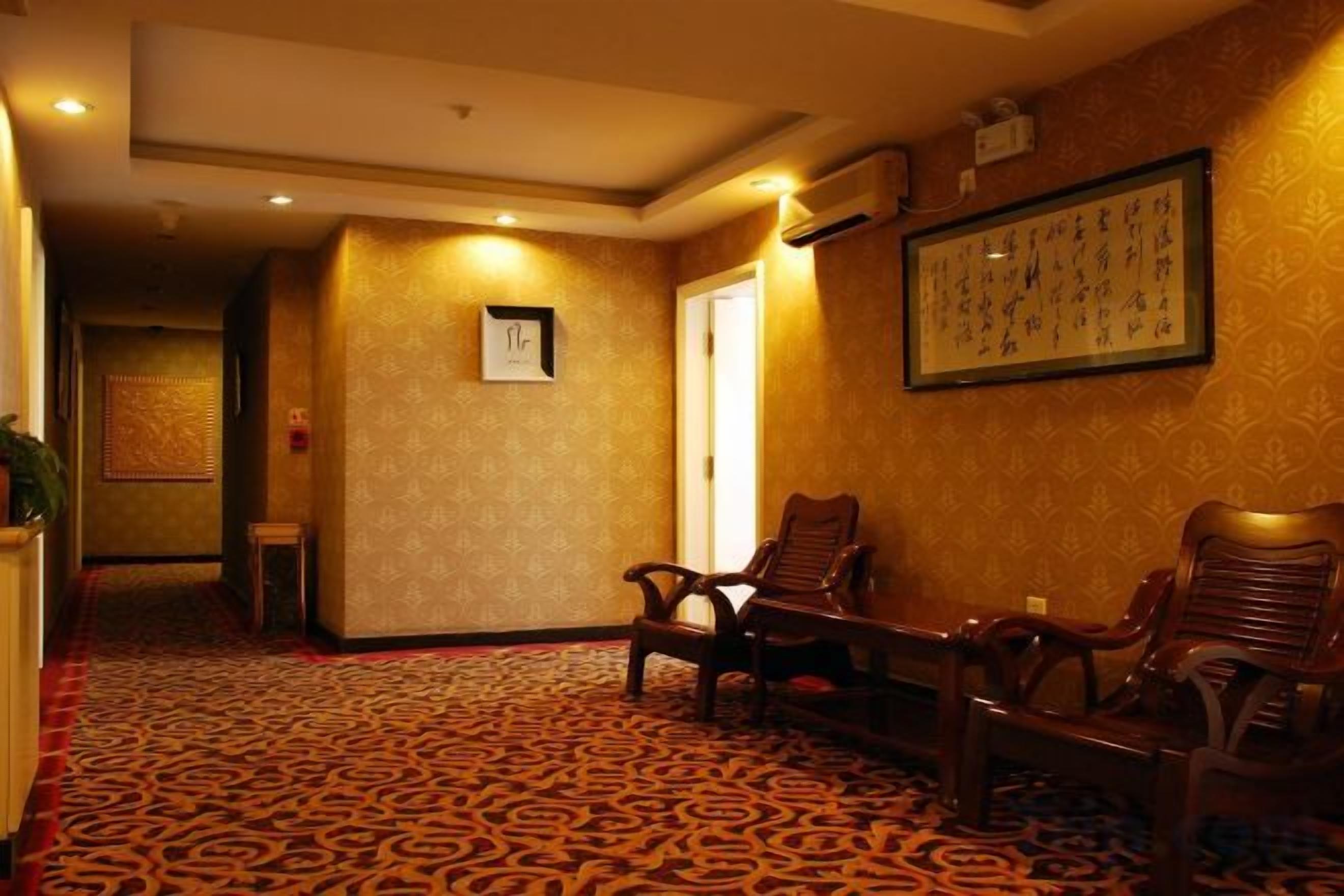 Vestíbulo de hotel con alfombra estampada, sillas de madera, una obra de arte enmarcada en la pared y una puerta que da a otra habitación.