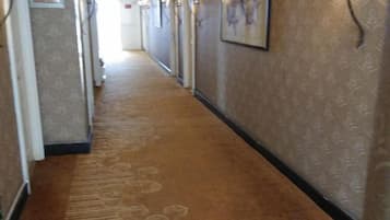 Un couloir recouvert de moquette, avec des portes sur le côté gauche et un tableau encadré sur le mur de droite.