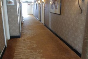 Un pasillo con alfombra, con puertas a la izquierda y un cuadro enmarcado en la pared derecha.