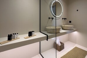 A modern bathroom with a round mirror, two vessel sinks, and a shelf with toiletries. - Bohemian Kea Beach Club Resort (Kea)