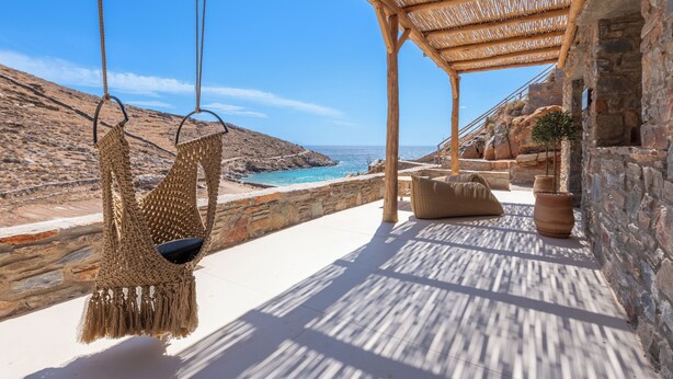 A beachside terrace with a hanging chair, stone walls, and a view of the sea. - Bohemian Kea Beach Club Resort (Kea)