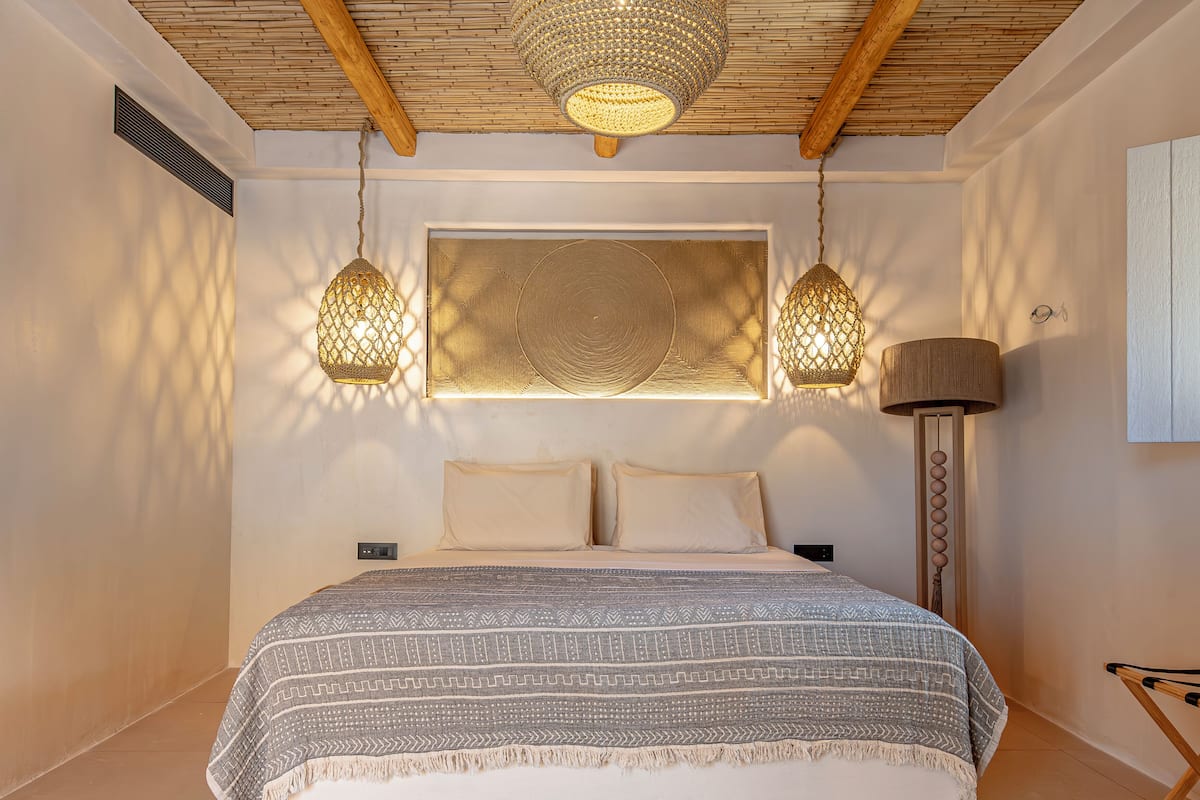 A bedroom with a bed, two hanging lamps, a wall-mounted light, and a floor lamp.