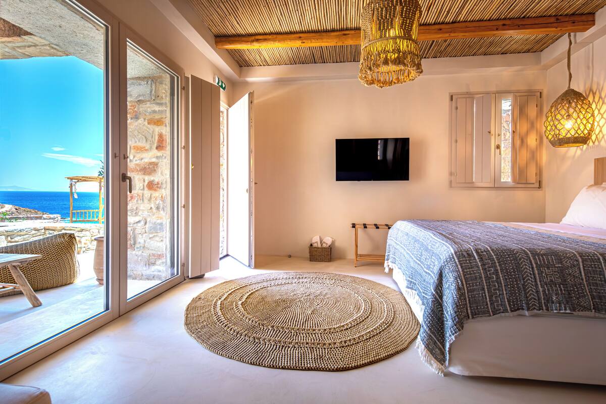 A bedroom with a large bed, a television, and a view of the sea through a glass door.