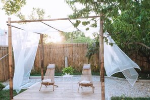 A wooden deck with two wicker chairs under a white canopy.