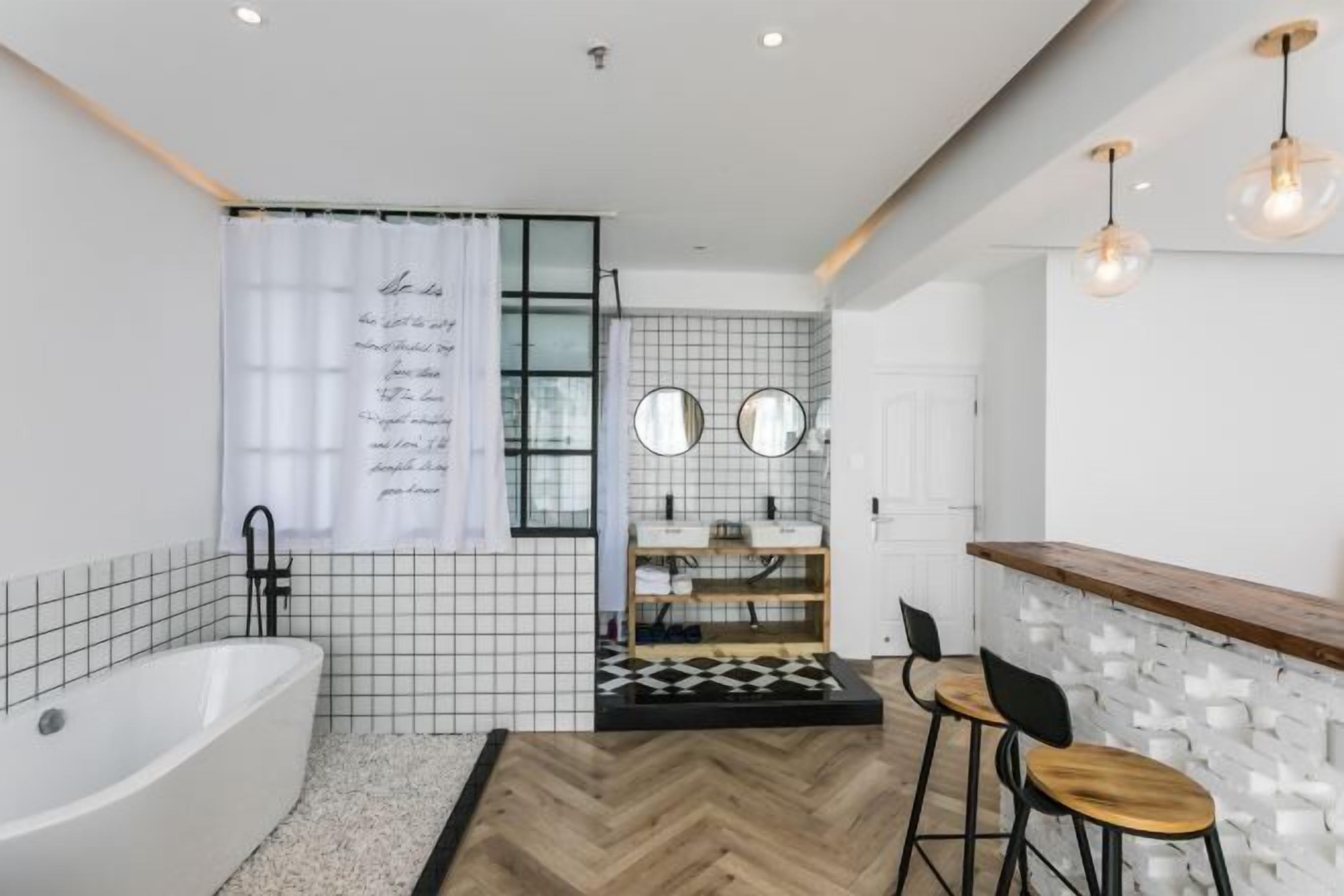 A modern bathroom with a bathtub, two mirrors, a sink, and a bar area with stools.
