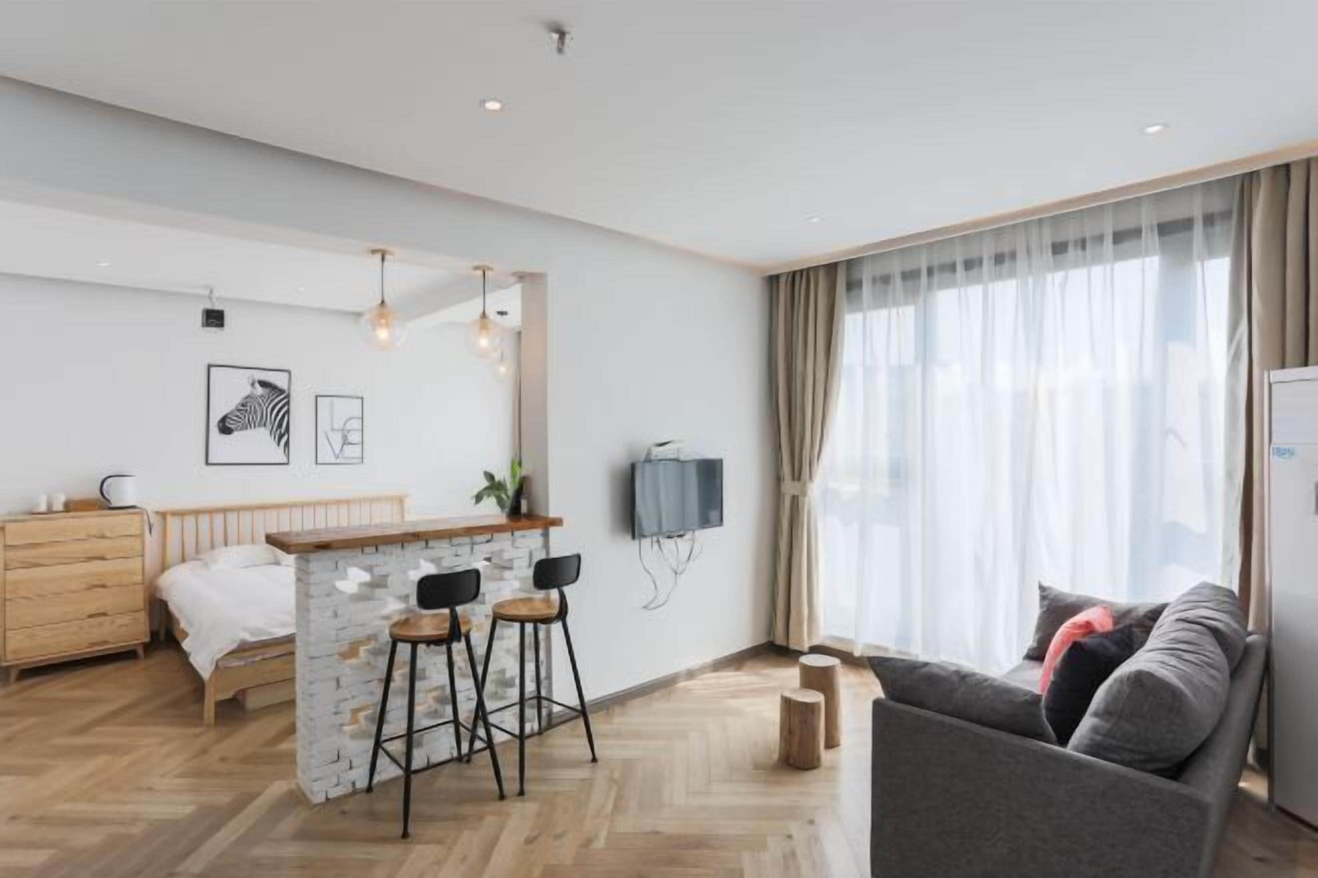 A modern hotel room with a bed, a small bar area, a sofa, and a TV mounted on the wall.
