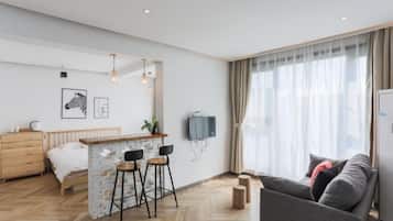 A modern hotel room with a bed, a small bar area, a sofa, and a TV mounted on the wall.