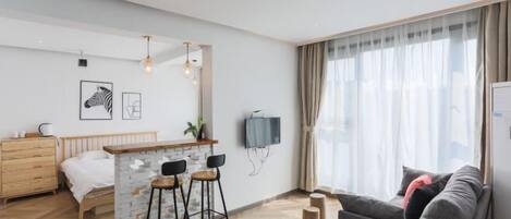 A modern hotel room with a bed, a small bar area, a sofa, and a TV mounted on the wall.