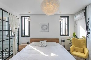 Een moderne hotelkamer met een groot bed, twee bedlampen, een plafondlamp, een nachtkastje, een stoel en een raam met gordijnen.