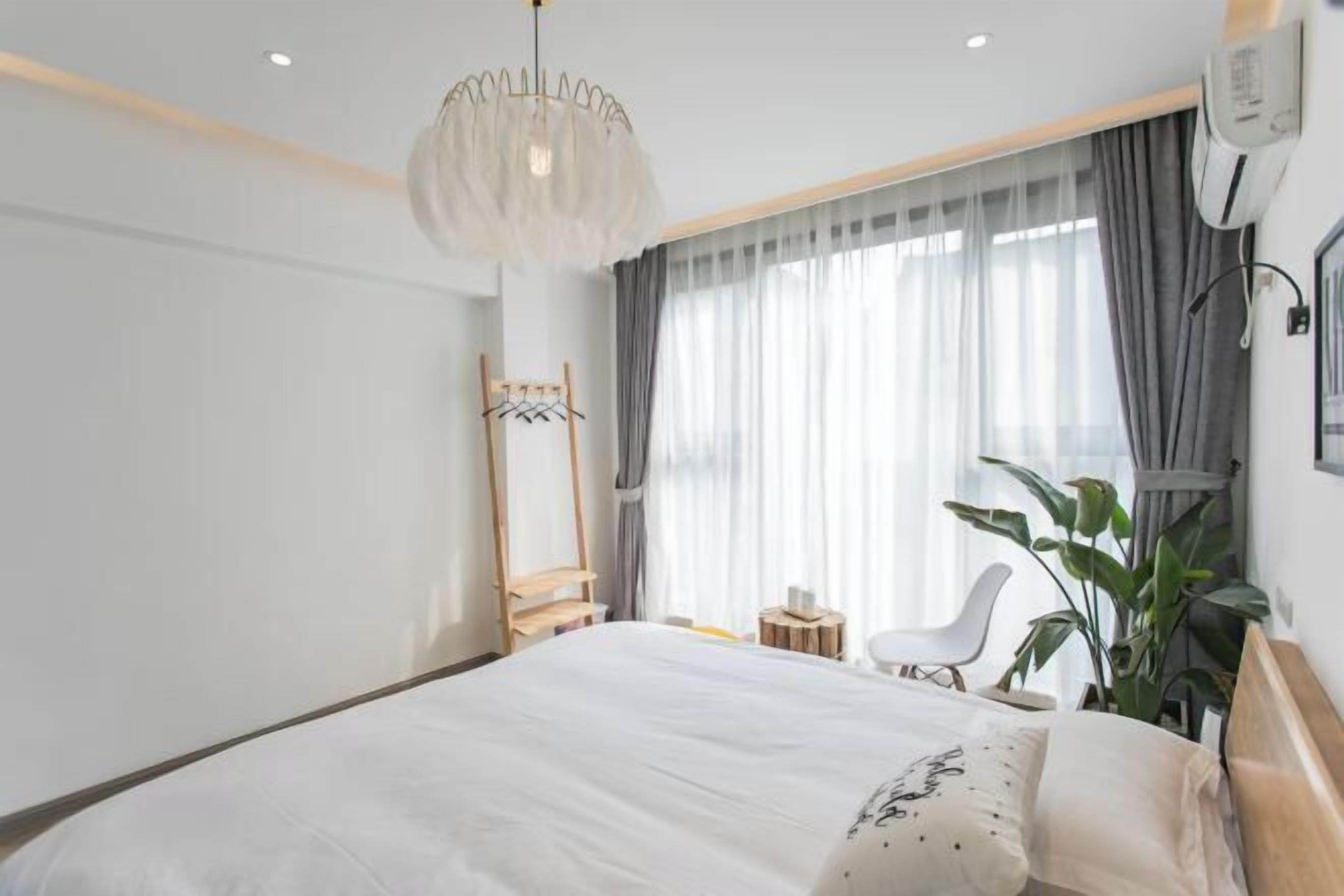A modern hotel room with a large bed, a hanging light fixture, a mirror, a chair, and a potted plant.