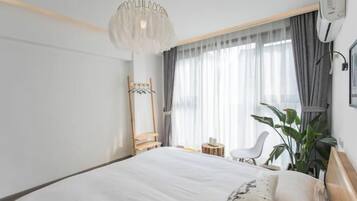 A modern hotel room with a large bed, a hanging light fixture, a mirror, a chair, and a potted plant.