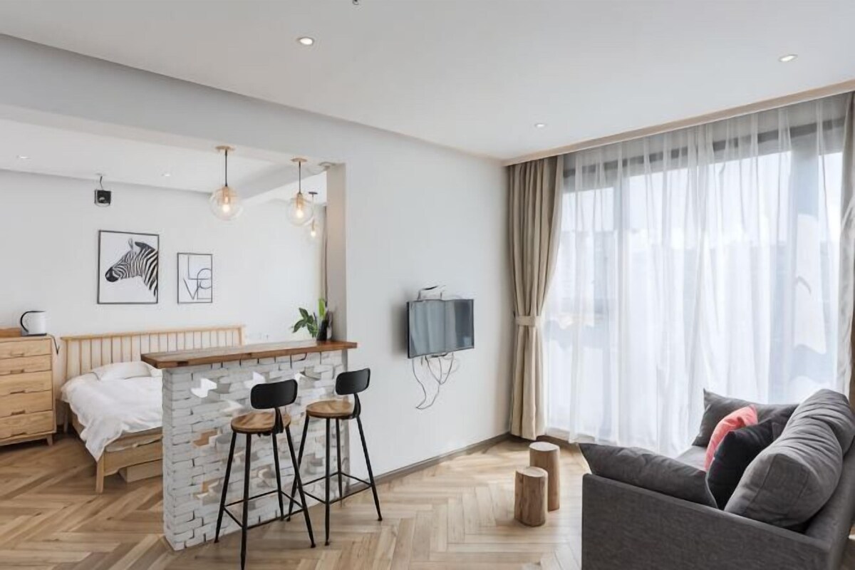 A modern living room with a stone accent wall, a bar area with stools, a sofa, and a television.