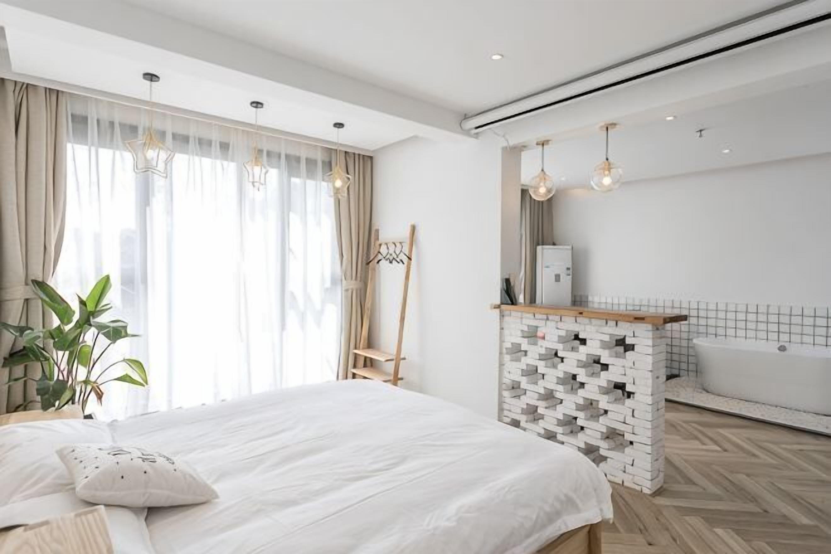 A modern bedroom with a bed, a plant, a wooden side table, a hanging light fixture, and a bathtub.