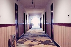 Ein Hotelgang mit Teppichmuster, Türen auf beiden Seiten und einem Mülleimer links.
