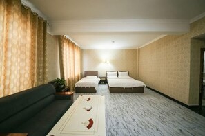 A hotel room with a sofa, two beds, a nightstand, a lamp, and a patterned carpet.