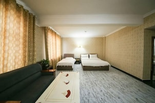 Una habitación de hotel con sofá, dos camas, una mesita de noche, lámpara y alfombra estampada.